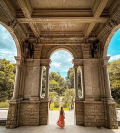 a woman in an orange dress is walking through the archways to a building with columns