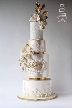 a three tiered wedding cake with white and gold flowers on it's side