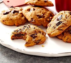 several chocolate chip cookies on a plate with a cup of coffee in the back ground