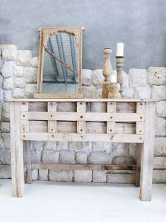 an old wooden table with a mirror and candles on it next to a stone wall