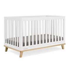 a white crib with wooden legs and a mattress in the bottom half, against a white background