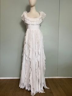 "Absolutely gorgeous white long 70s cotton dress. Has a scooped neckline with a double tiered frill that can be worn off the shoulders, a waist seam that measures 30\" and a long floaty skirt with vertical tiers along the length of the skirt. Fastens not he side with buttons. Fully lined in white cotton and has well constructed bodice for better fit and comfort. Would make a fabulous wedding dress! Size UK 8/10" White Tiered Dress With Ruffles, White Maxi Dress With Ruffled Skirt, White Tiered Maxi Dress With Ruffles, White Tiered Ruffle Dress, White Tiered Ruffle Maxi Dress, White Tiered Dress With Ruffled Straps, Flowy Cotton Maxi Dress With Ruffles, White Ruffled Tiered Dress For Garden Party, White Tiered Ruffle Dress For Garden Party