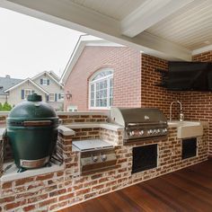 an outdoor kitchen with grill and television on brick wall, wood flooring and hard wood floors