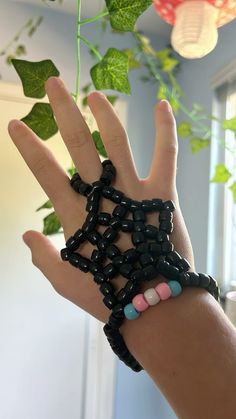 a person's hand holding up a bracelet made out of black beads and green leaves