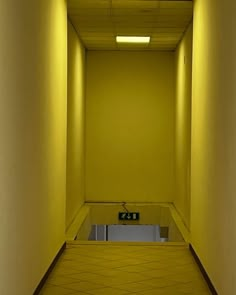 an empty hallway with yellow walls and tile flooring is lit by recessed lights