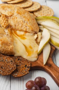 an apple and cheese sandwich on a cutting board with crackers, grapes and apples