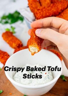 a person dipping something into a small white bowl filled with ranch dressing on top of a wooden cutting board