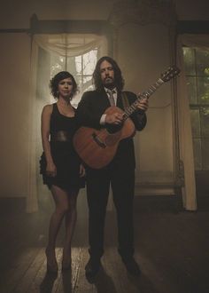 a man and woman standing next to each other holding an acoustic guitar