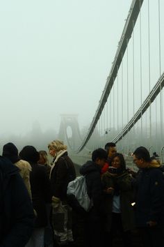 a group of people standing in front of a bridge on a foggy day,