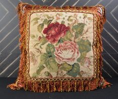 a decorative pillow with tassels and flowers on the front, sitting on a black surface