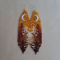 an orange and white owl beaded earrings with crescent moon on the front, sitting on a beige surface