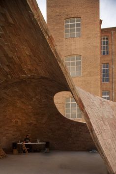 a person sitting at a table in front of a large brick building with two windows