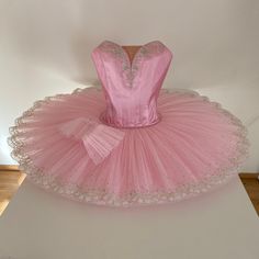 a pink ballerina dress sitting on top of a white table next to a wall