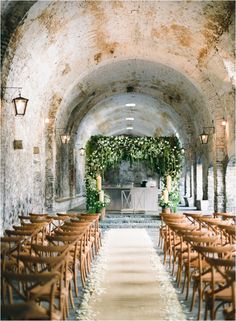 rows of wooden chairs are lined up in an old stone building with ivy growing on the ceiling