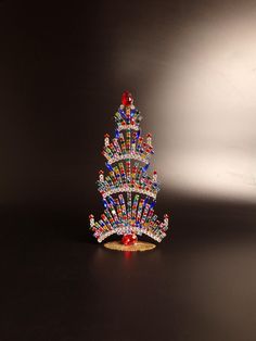 a small christmas tree made out of beads on a black surface with a white background