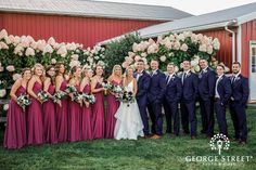 a group of people standing next to each other in front of a red building with white flowers