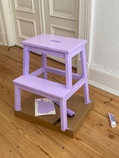 a purple step stool sitting on top of a cardboard box in front of a door