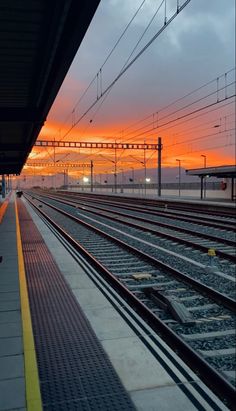 the sun is setting at an empty train station with many tracks in front of it