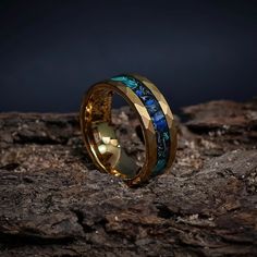 a gold ring with blue and green stones inlayed to it on top of a rock