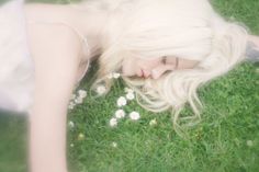 a woman laying in the grass with her hair blowing back and eyes closed to the camera