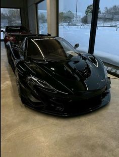 a black sports car parked in front of a large window with snow on the ground