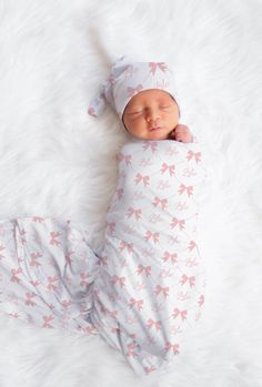 a baby sleeping on top of a white blanket wearing a pink bow hat and swaddle