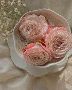 three pink roses are in a white bowl on a bed with some baby's breath flowers