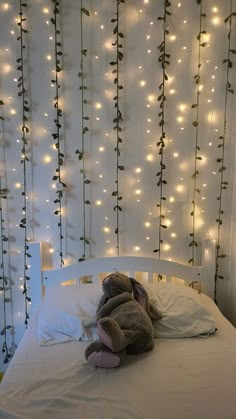 a teddy bear laying on top of a white bed in front of a wall with lights