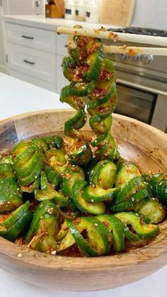 a wooden bowl filled with green peppers on top of a white counter next to an oven