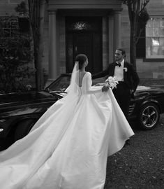 a bride and groom standing in front of a classic black car on their wedding day