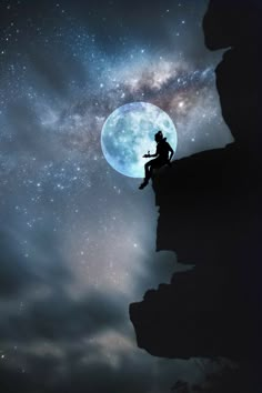 a man sitting on top of a cliff under a full moon