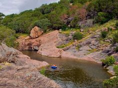 a person in a small boat on a river surrounded by rocks and greenery with trees