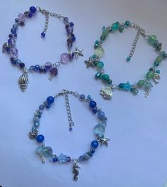 three bracelets with charms and beads on a white table top, one has a starfish charm