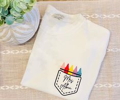 a white t - shirt with an image of a rainbow crayons in a pocket