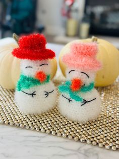 two knitted snowmen sitting next to each other on top of a table with pumpkins in the background