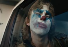 a man with his face painted like a clown is sitting in the back seat of a car