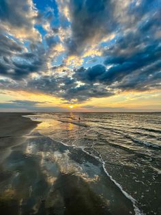 the sun is setting at the beach with people walking in the water