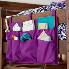 a purple bag hanging on the side of a bed with notes and pens in it