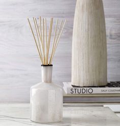 a white vase with reeds in it sitting on a table next to some books