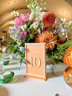 the table numbers are displayed on an orange and pink centerpiece with flowers in it