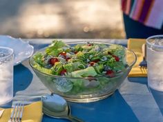 a salad in a glass bowl on top of a blue table cloth with silverware