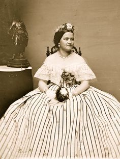 an old black and white photo of a woman in a striped dress sitting on a chair