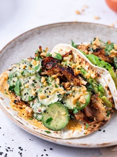 two tacos on a plate topped with cucumbers and other toppings, ready to be eaten