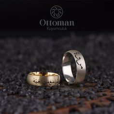 two gold wedding rings with arabic writing on them sitting on the ground in front of black gravel