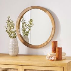 a round mirror sitting on top of a wooden dresser next to a vase filled with flowers