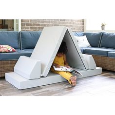 a woman sitting on the floor reading a book in a tent shaped like a couch