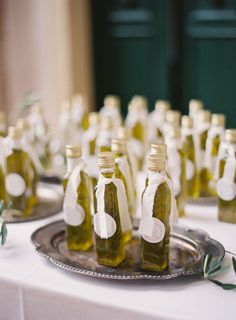 several bottles of olive oil sit on a silver platter with white ribbon around them