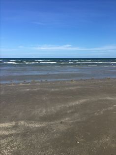 an empty beach with waves coming in from the ocean and blue sky above, on a sunny day