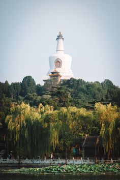 a large white building sitting on top of a lush green hillside next to a lake