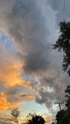 the sky is filled with clouds as the sun goes down in the distance behind some trees